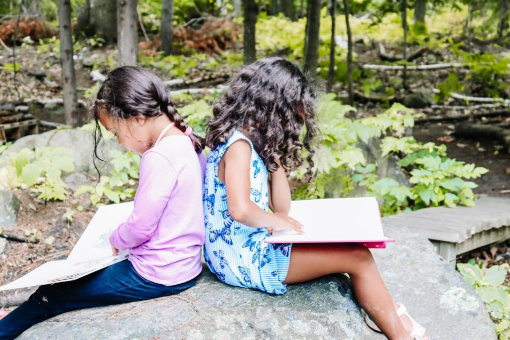 two little girls reading books while sitting on a rock